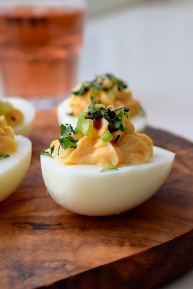Asian devilled eggs with miso and black sesame seeds close up on a wooden serving board.