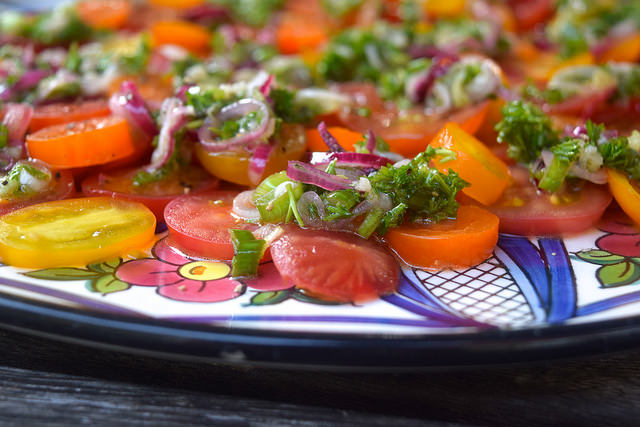 Close up of a tomato salad topped with herby dressing with sliced red shallots.