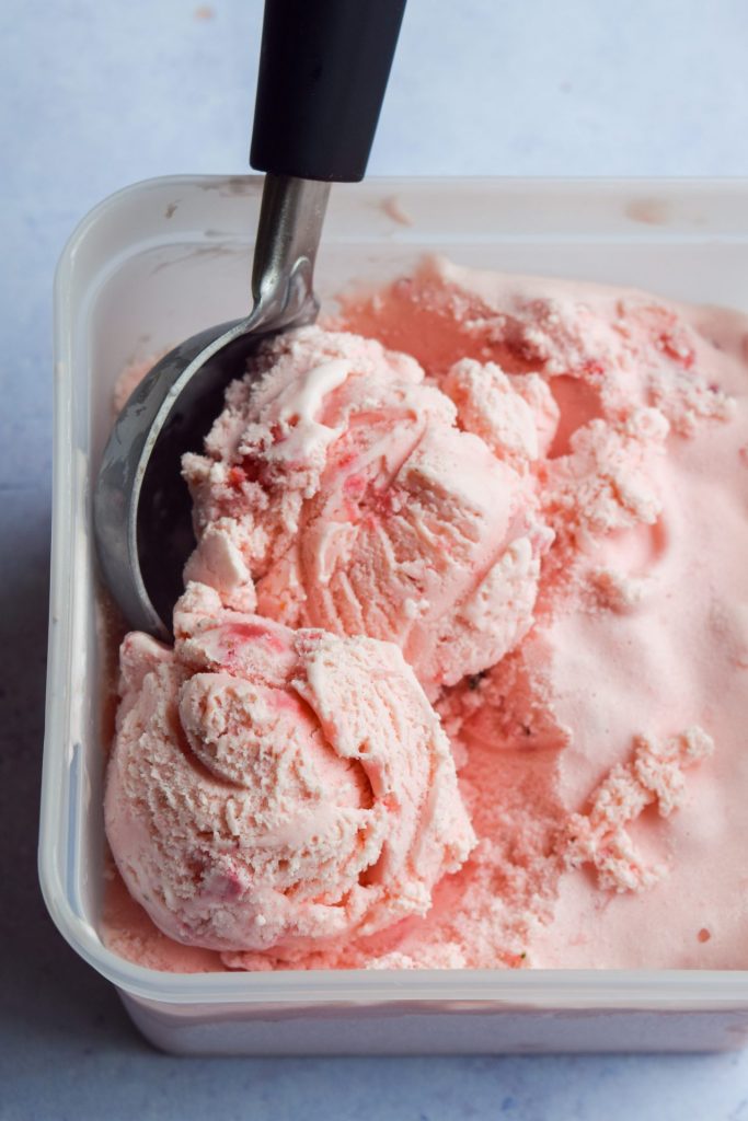 Ice cream scoop making scoops of strawberry ice cream from a plastic tub.