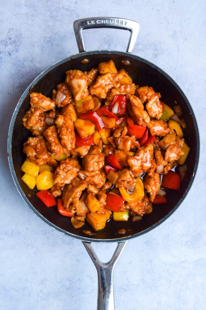Frying pan of sweet and sour chicken on a blue background.