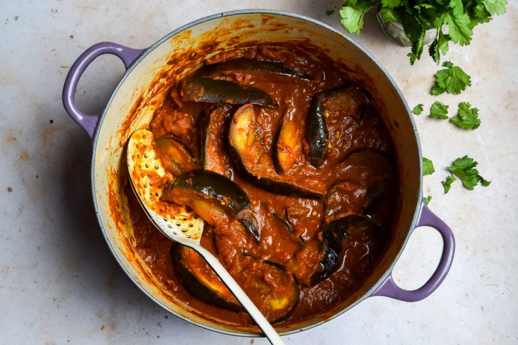 Tomato and aubergine curry pictured top down in a purple casserole dish.