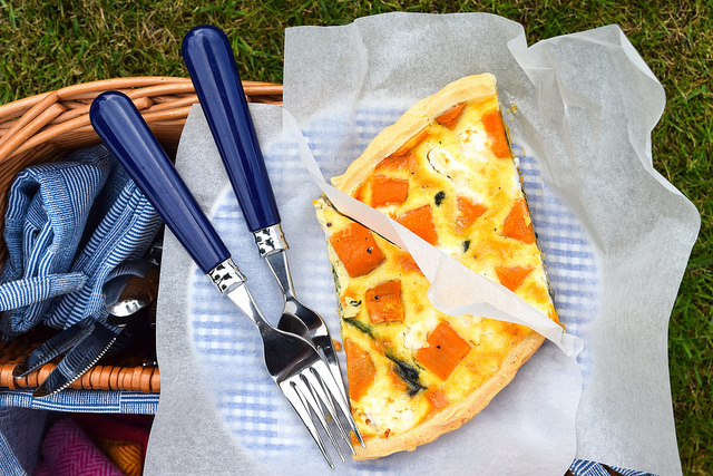 Slice of Sweet Potato, Red Onion, Spinach & Feta Quiche on top of a picnic basket.