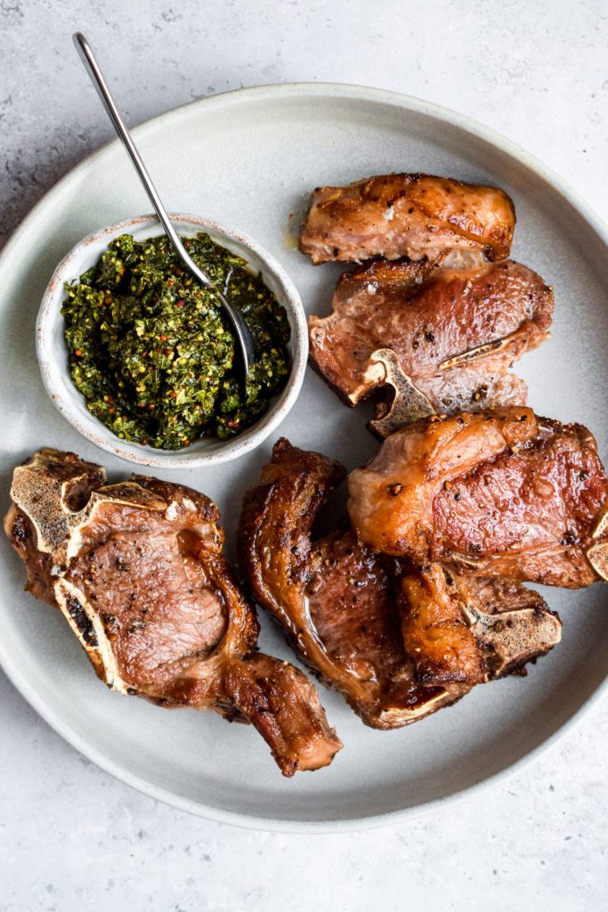 Plate of pan fried chops and a grey bowl of mint sauce.