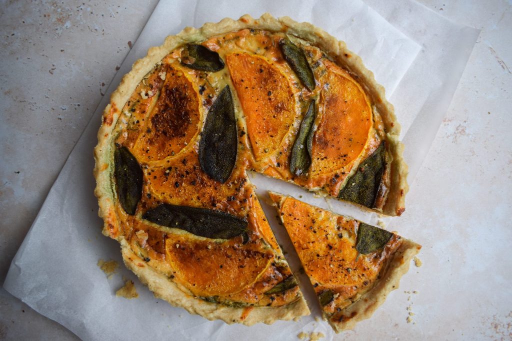 Squash tart topped with sage leaves on a piece of baking parchment.