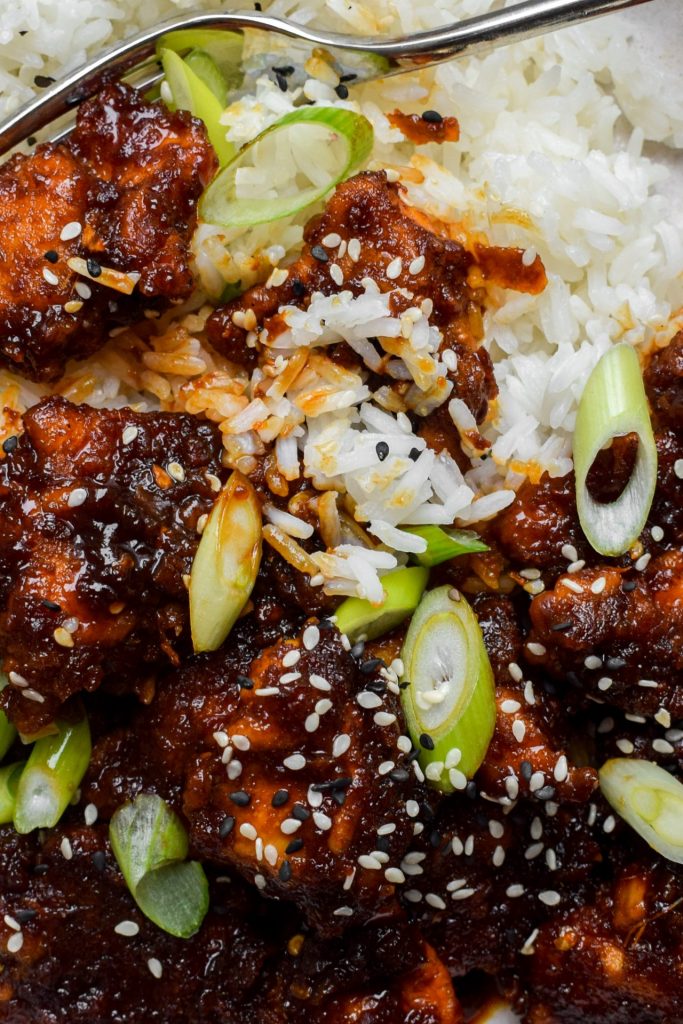 Close up of Chinese orange chicken with rice, sesame seeds and sliced spring onions.