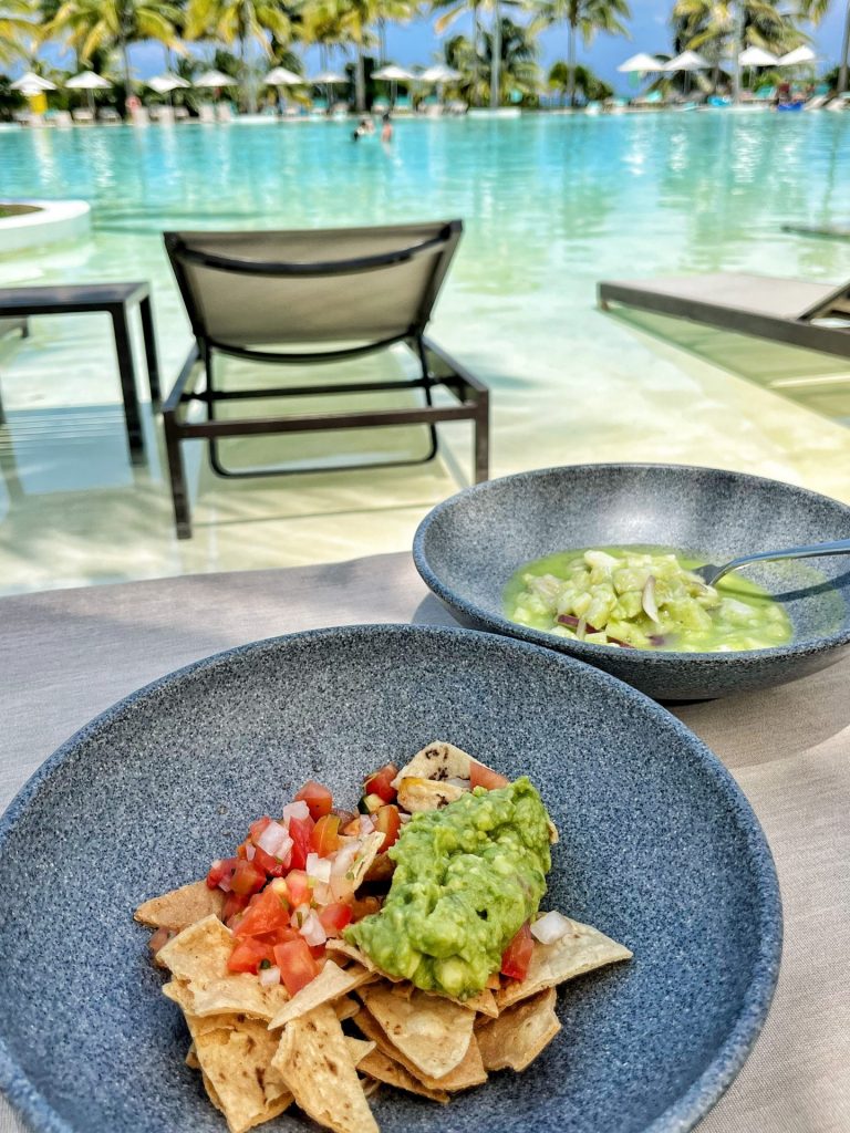 Bowls of tortilla chips, salsa, guacamole and ceviche by a swimming pool.