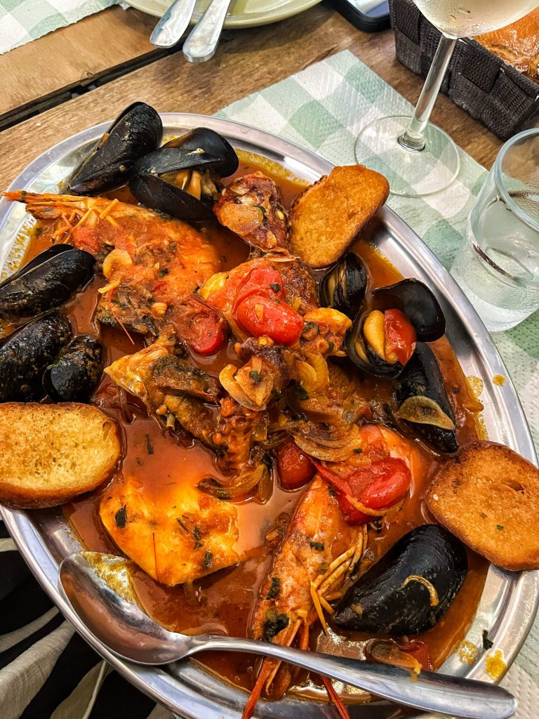 Large silver platter of mussels, prawns, and fish in a cherry tomato sauce.