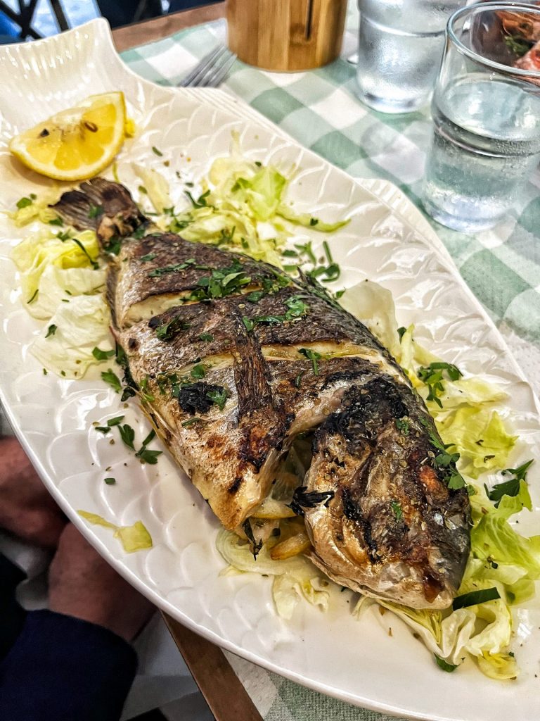 Whole grilled sea bream on a white serving platter with a lemon wedge and shredded lettuce.