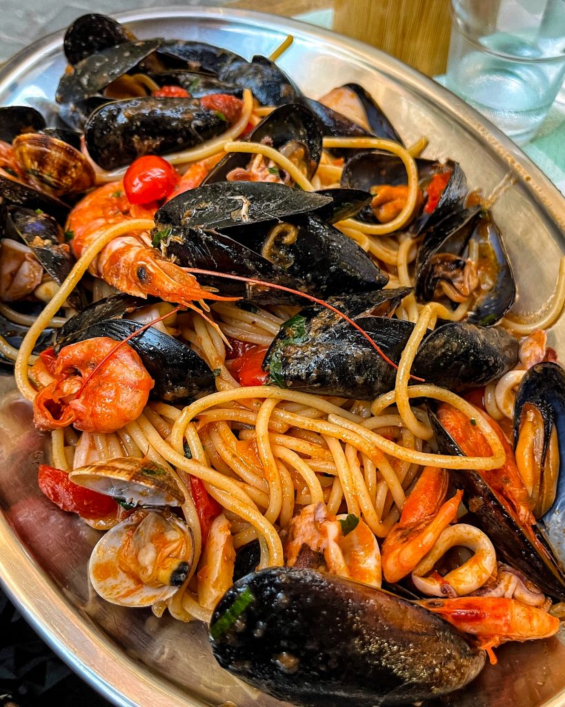 Metal serving platter of tomato spaghetti with mixed seafood.