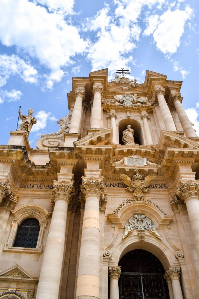 Facade of Syracuse Cathedral against a cloudy blue sky.