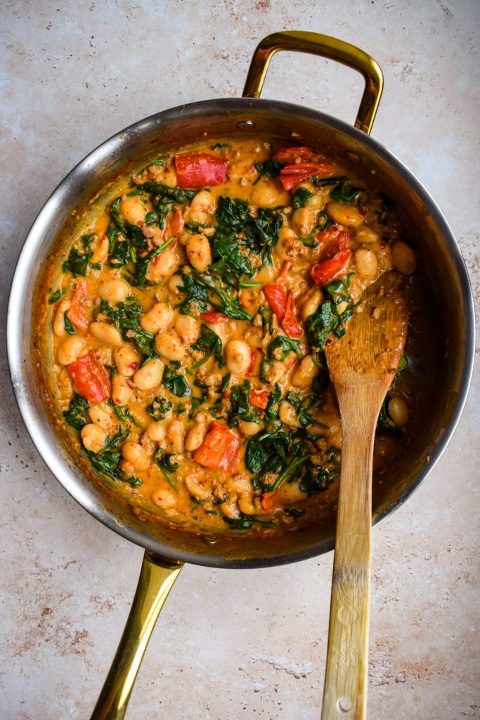 Gold and silver skillet of creamy spinach and pepper butter beans.