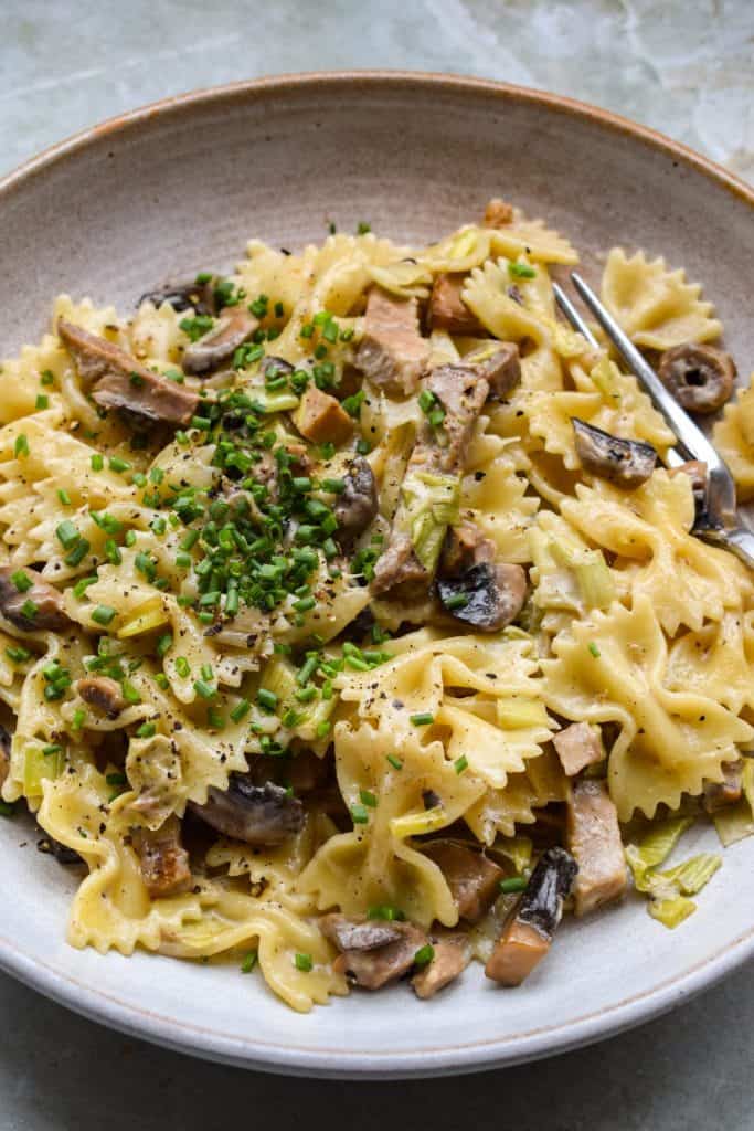 Close up of a bowl of leftover roast pork pasta with mushrooms, leeks and chives.