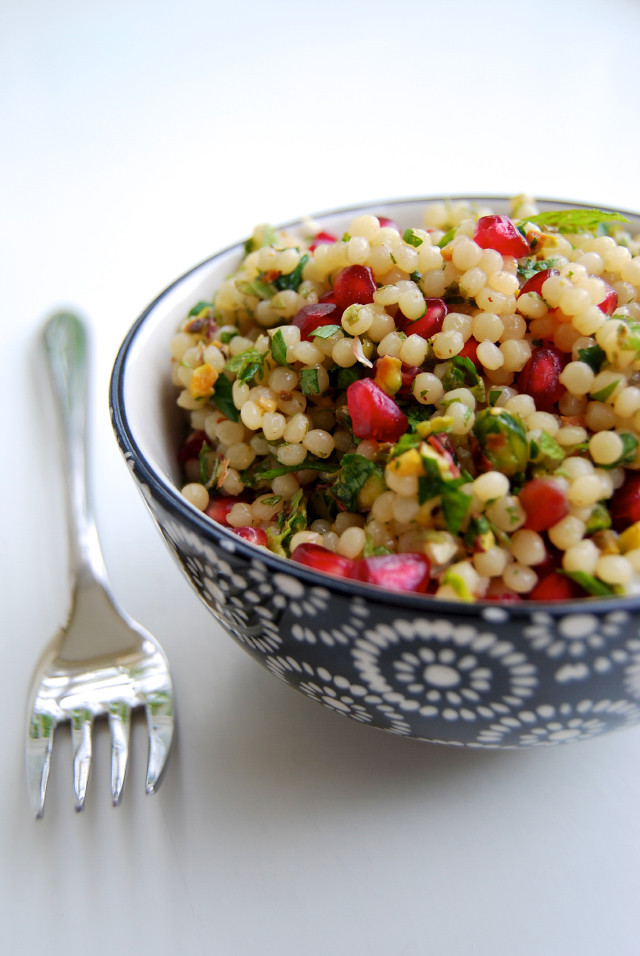 Close up of a bowl of giant couscous with pomegranate and pistachios.