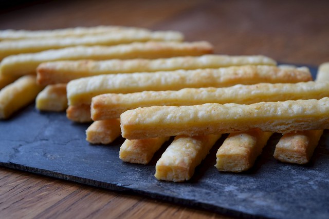 Two layers of cheese straws stacked on top of each other on a piece of slate.