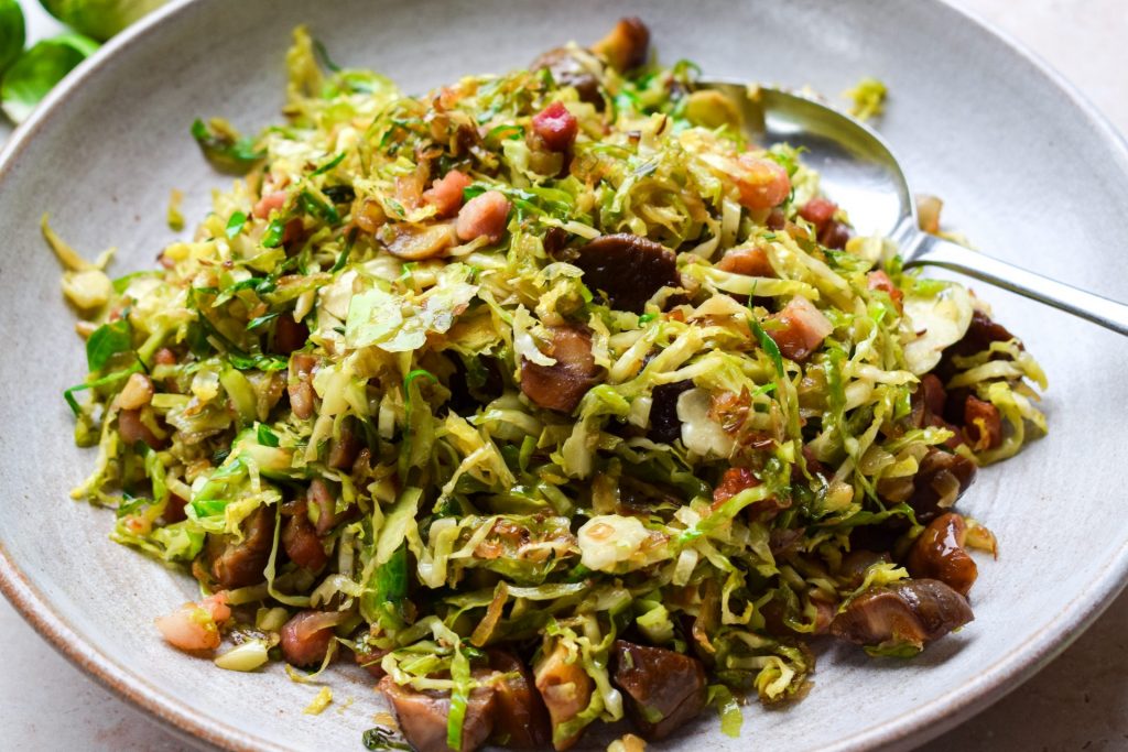 Grey bowl of shredded cooked brussels sprouts with a spoon in the side.