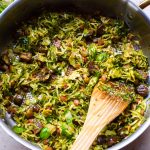 Pan of shredded sprouts being stirred with a wooden spatula.