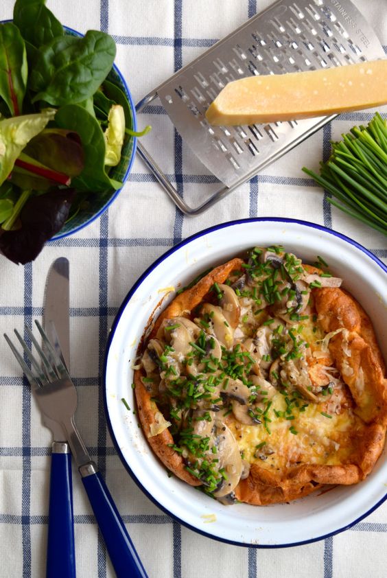 Overhead image of a dutch baby pancake in a blue and white dish topped with creamy sliced mushrooms and chives.