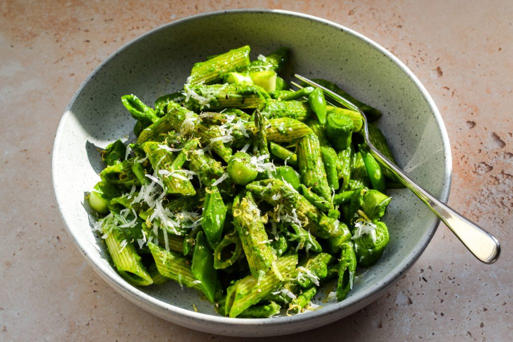 Grey bowl with a fork of penne tossed in a smooth pesto. 