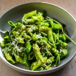Grey bowl with a fork of penne tossed in a smooth pesto.