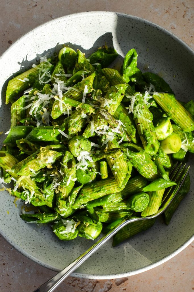 Close up of spinach pesto penne with spring vegetables pictured in direct sunlight.
