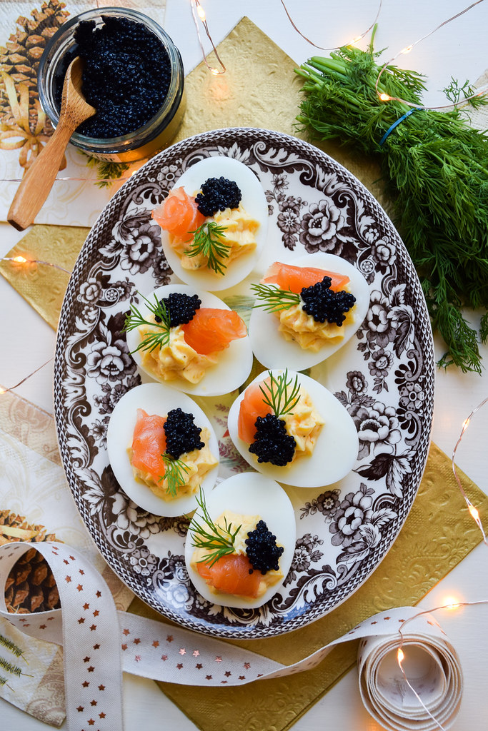 Overhead view of six devilled eggs royale with smoked salmon and caviar. The pot of caviar is off to one side as is a bunch of dill.