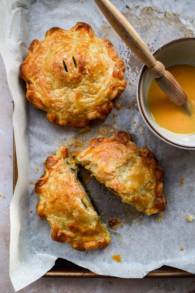 Two individual mushroom wellingtons on a baking sheet with one cut in half.
