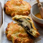 Mushroom wellington sliced in half on a baking sheet with another whole one and a bowl of egg wash in the background.