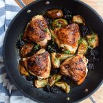 Close up of roasted chicken, apples and prunes in a shallow casserole.