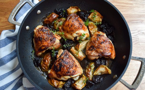 Shallow casserole of roasted chicken thighs, apples and prunes scattered with fresh thyme sprigs.