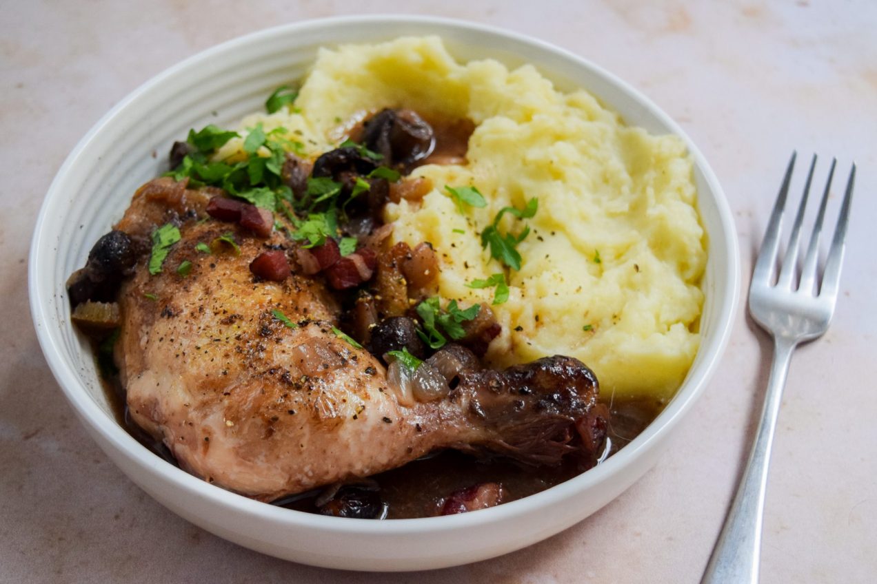 Chicken leg coq au vin with mashed potatoes and chopped parsley in a white bowl.