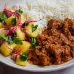Close up of a lamb curry with a pineapple salad and rice.
