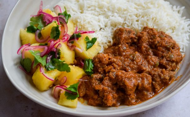 Close up of a lamb curry with a pineapple salad and rice.
