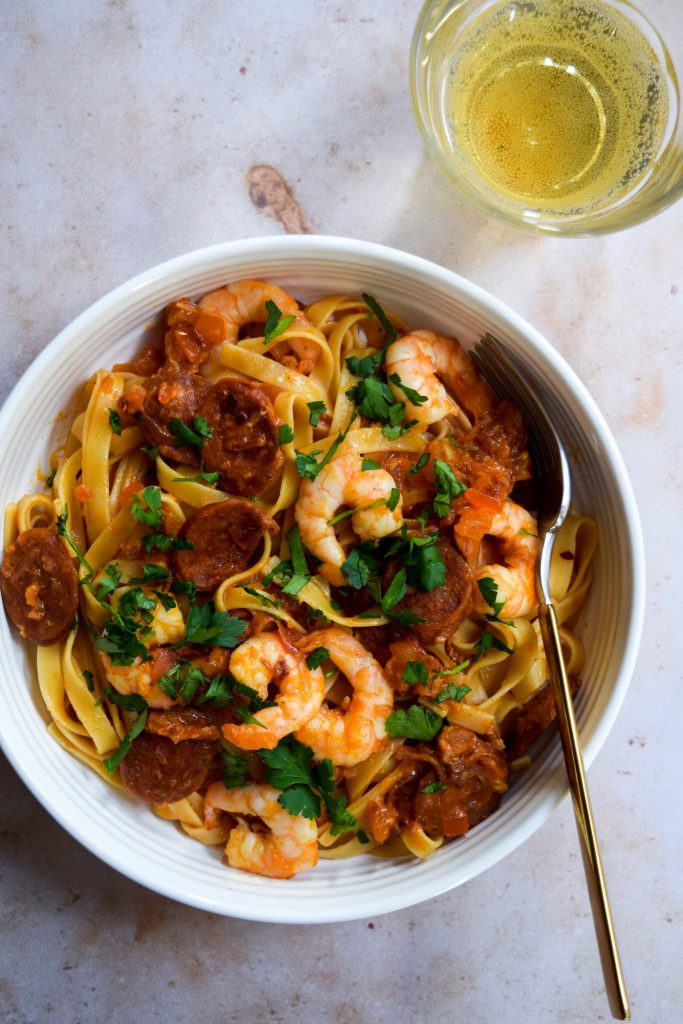 Prawn and Chorizo Pasta garnished with parsley in a white bowl on a stone background.