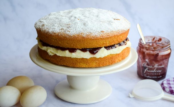 Cake filled with jam and buttercream on a white cake stand.