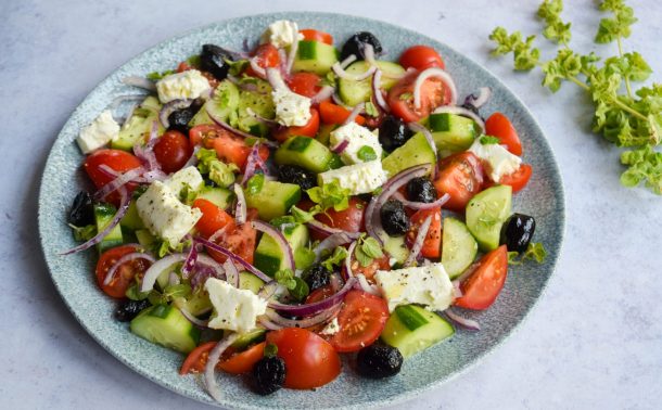 Side on view of a greek salad with feta, onions, cucumber, olives and tomato on a blue plate.