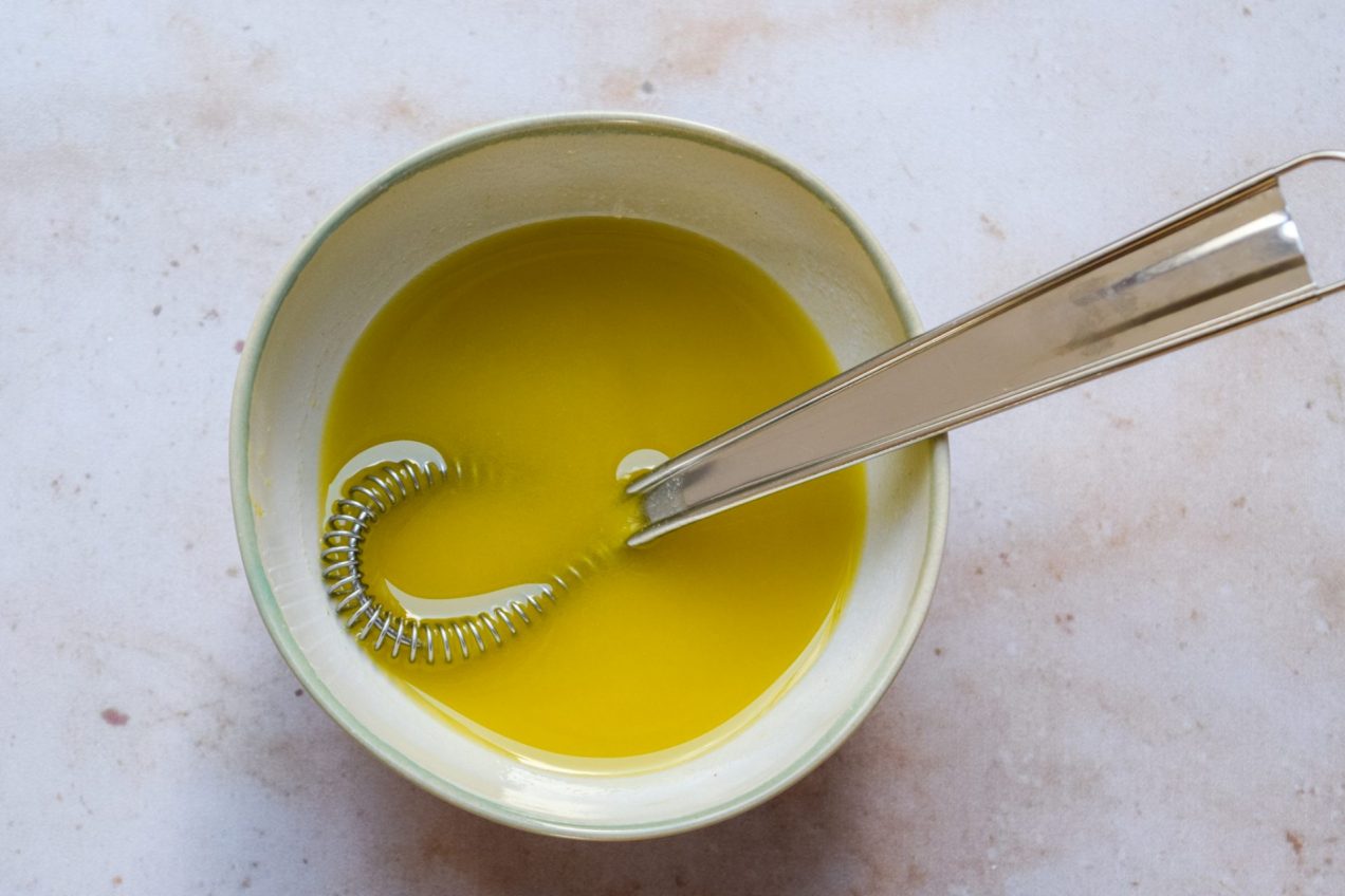 Bowl of truffle vinaigrette being whisked on a neutral background.