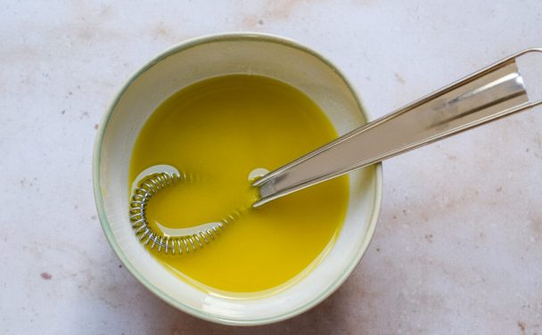 Bowl of truffle vinaigrette being whisked on a neutral background.