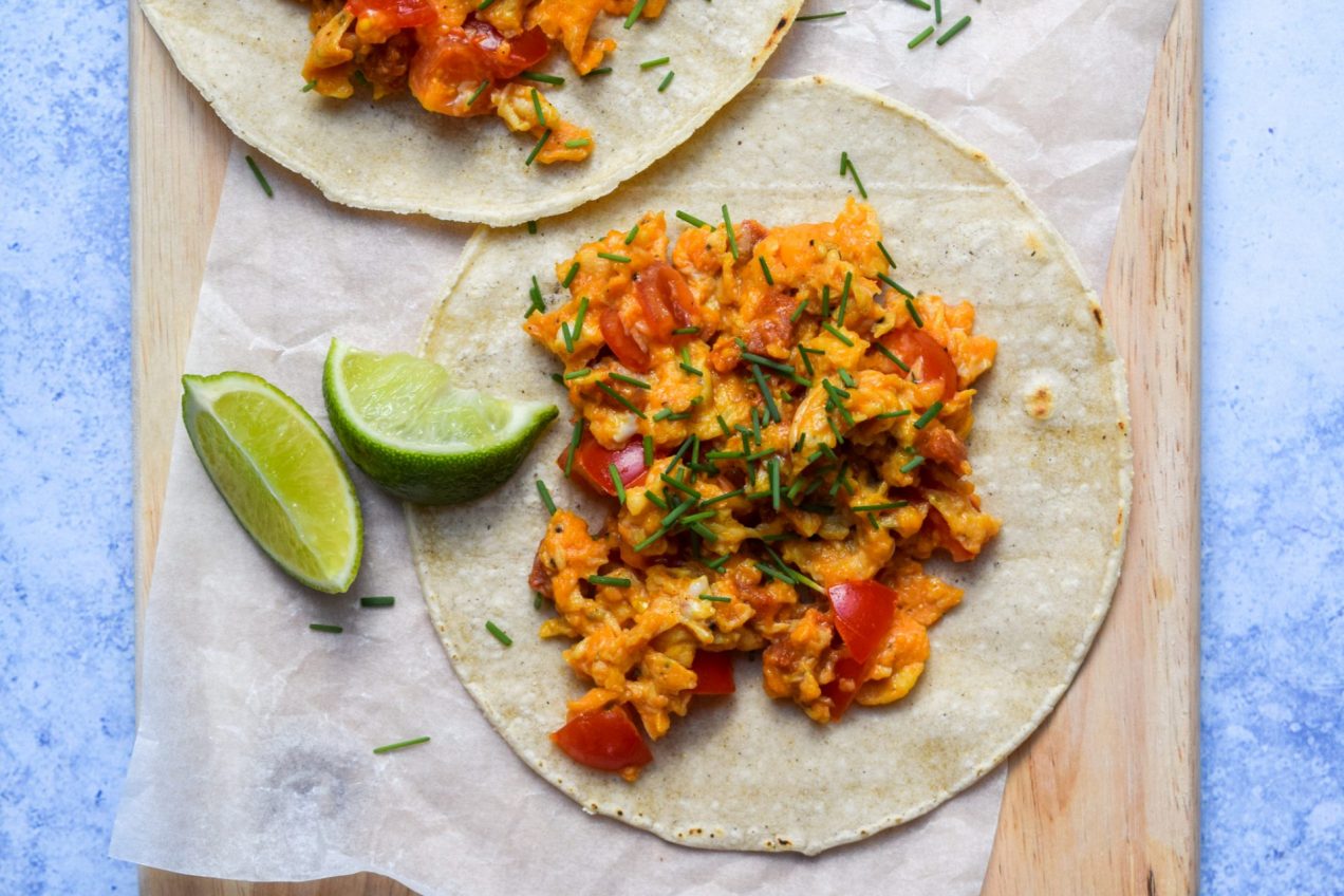Egg, tomato and chorizo taco on a serving board with two lime wedges.
