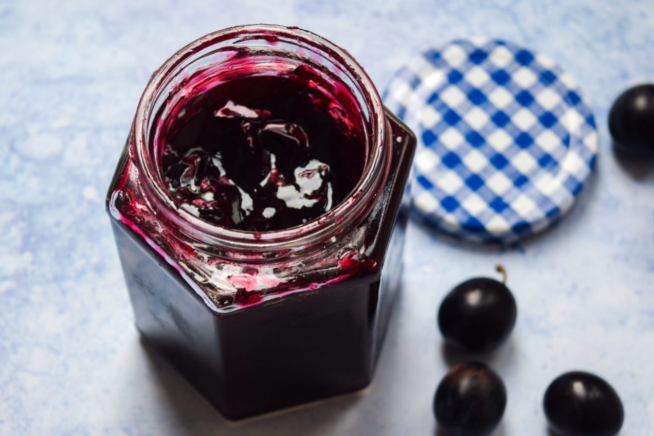 Open jar of damson jam on a blue background.