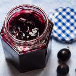 Open jar of damson jam on a blue background.