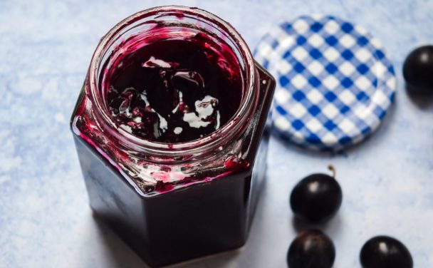 Open jar of damson jam on a blue background.