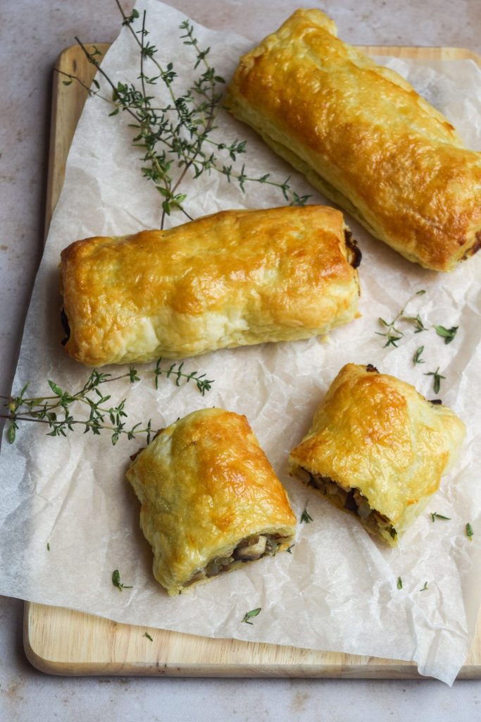 Mushroom sausage rolls on a baking parchment lined wooden board.