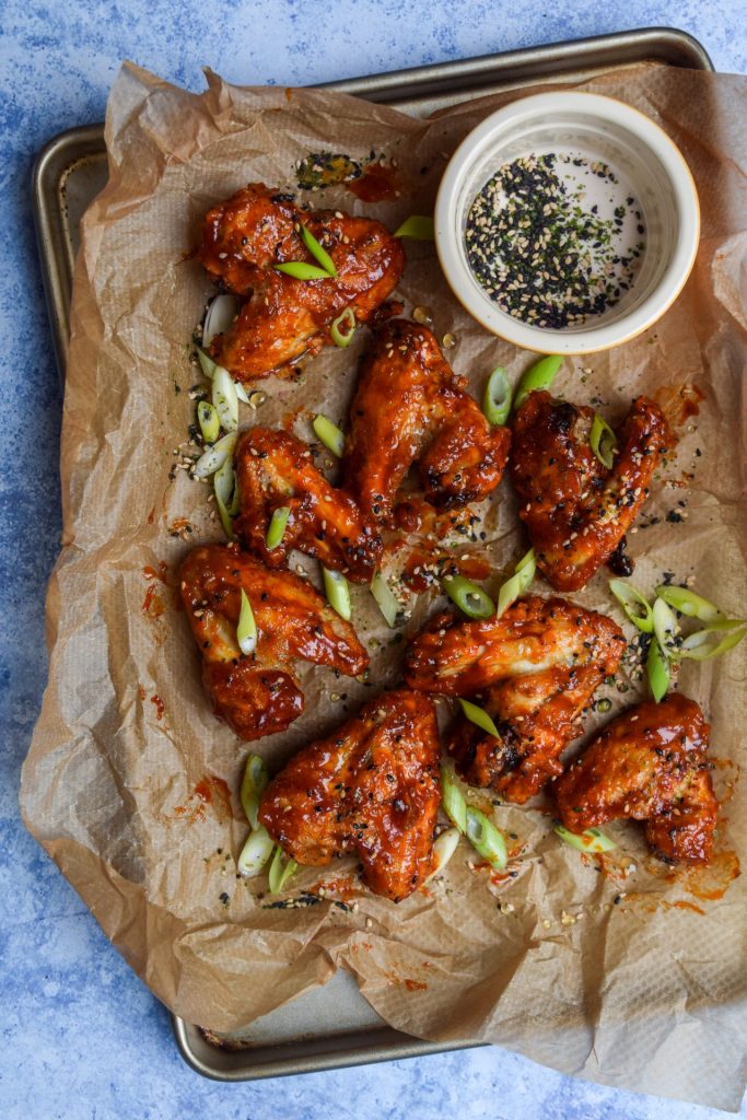 Korean Fried Chicken Wings on a tray lined with brown baking paper and sprinkled with furikake and sliced spring onions.