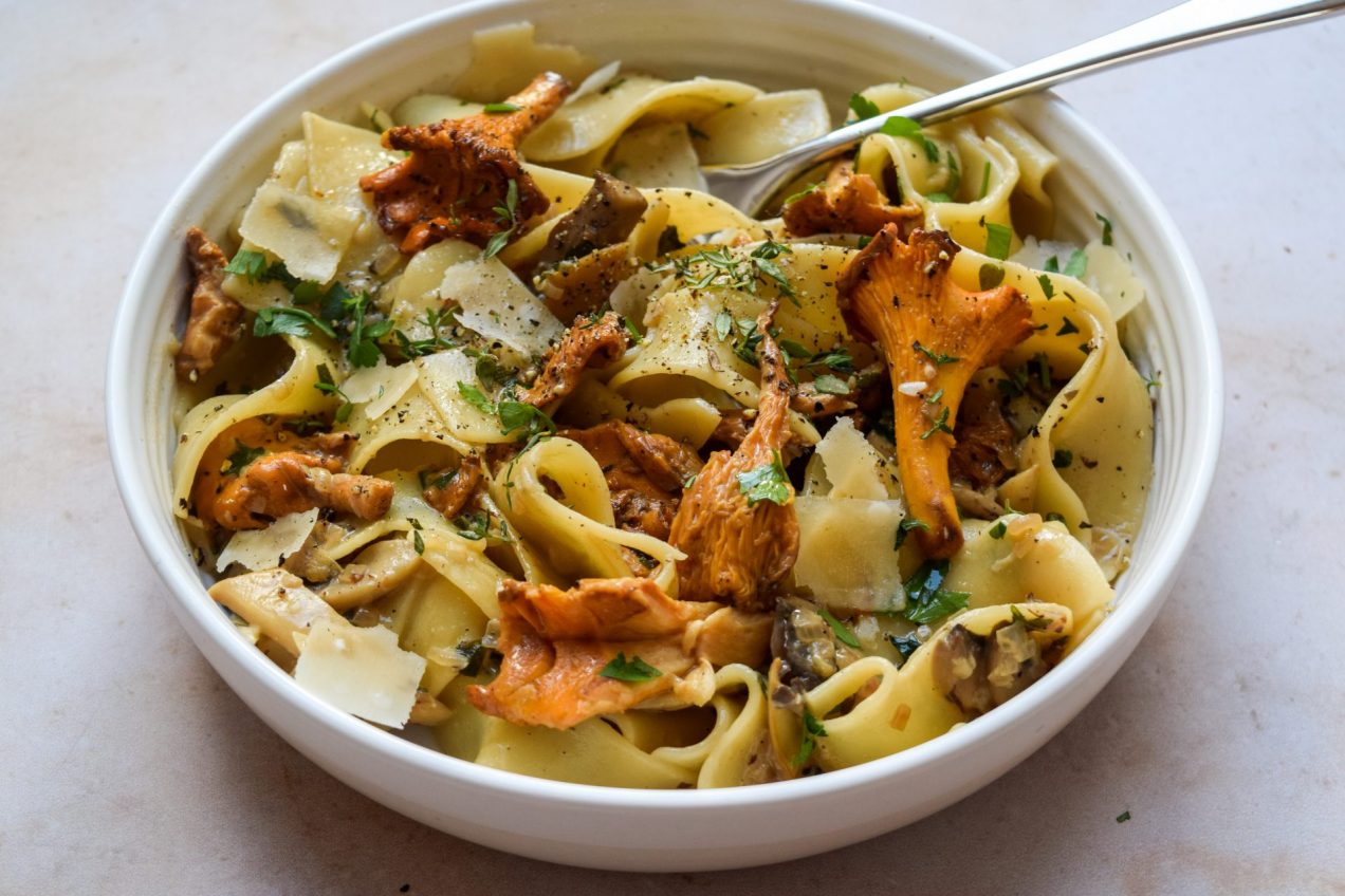 White bowl of wild mushroom pappardelle with plenty of fresh thyme and parmesan shavings sprinkled on top.