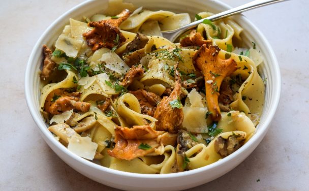 White bowl of wild mushroom pappardelle with plenty of fresh thyme and parmesan shavings sprinkled on top.