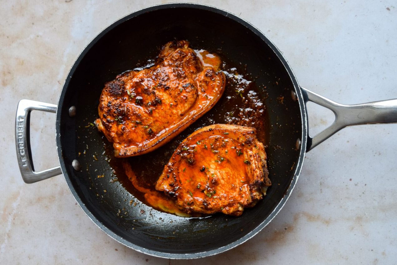 Le Creuset frying pan with two pork chops cooked in paprika butter.