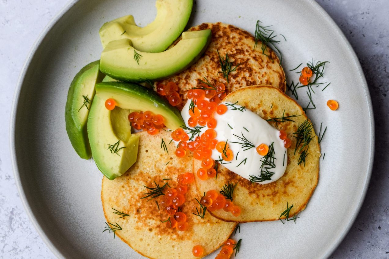 Matzo meal pancakes on a grey plate with avocado, soured cream, dill and salmon roe.