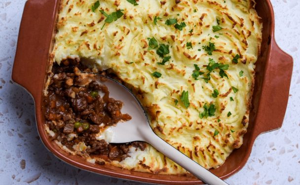 A brown dish of cottage pie with a spoon serving a portion to show the meat filling.