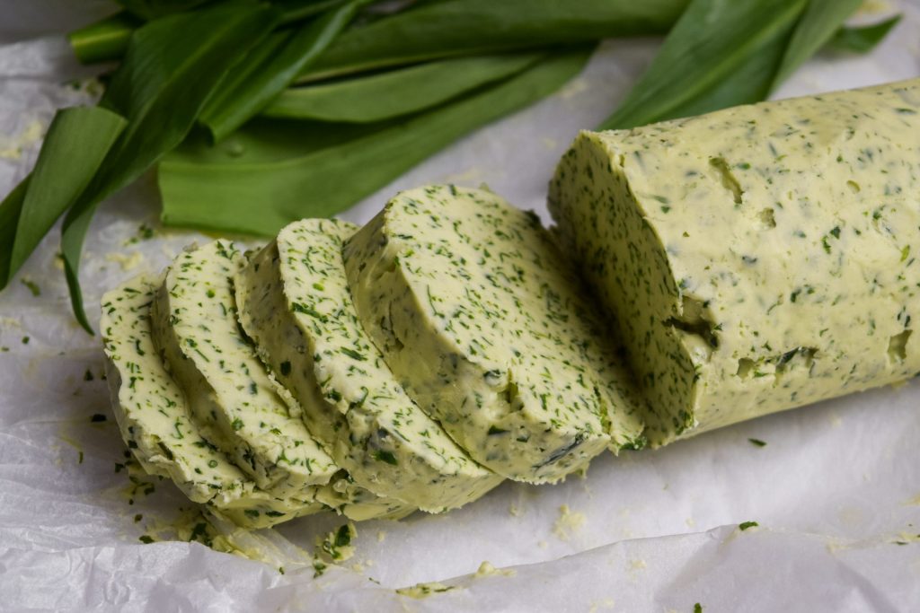 Log of wild garlic butter slice with wild garlic leaves in the background.