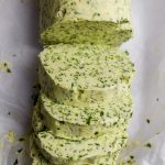 Sliced log of wild garlic butter on a piece of baking parchment.